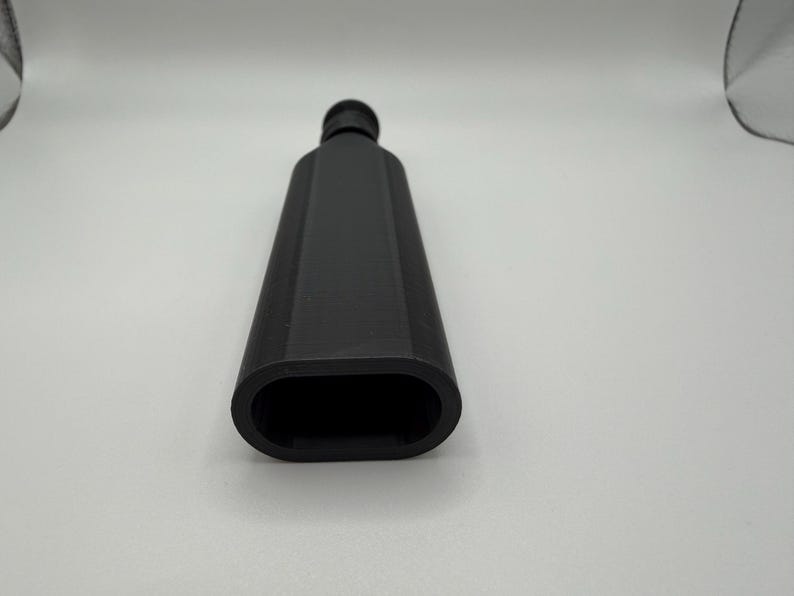 Puede incluir: Una botella negra rectangular con una abertura ovalada redondeada. La botella tiene un cuello estrecho y un acabado liso y mate. El objeto est&aacute; sobre un fondo blanco.