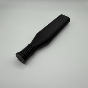 Puede incluir: Un tap&oacute;n de botella negro con una parte superior rectangular y una base acanalada. El tap&oacute;n tiene un cuerpo largo y rectangular y est&aacute; dise&ntilde;ado para encajar en una botella. El tap&oacute;n est&aacute; hecho de un material negro mate.