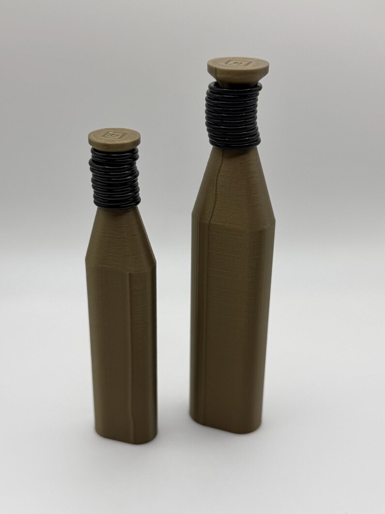 May include: Two brown bottles with black, ridged necks and flat, circular tops. The bottles are different sizes, with the larger one standing taller than the other. The bottles are set against a plain, light background.