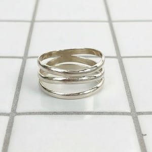 May include: A silver ring with a layered design. The ring features three bands that are connected, creating a unique and modern look. The ring is made of a shiny, metallic material.