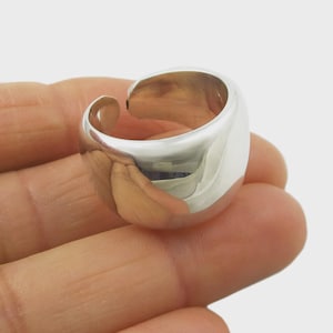 May include: A shiny, silver-colored ring with a rounded, thick band and an open design. The ring has a smooth, polished surface, reflecting light. The ring is a statement piece, suitable for everyday wear or special occasions.