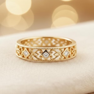 以下が含まれることがあります： 金色のリングで、精巧な透かし彫りのデザインが施されています。リングには、小さな透明な宝石をそれぞれ収めた、ひし形のセッティングが施されています。バンドは繊細なオープンワークのデザインで、レースのような効果を生み出しています。