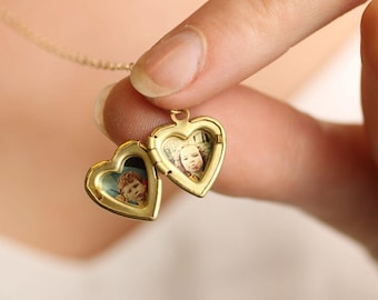 May include: A gold-toned heart-shaped locket pendant suspended from a delicate chain. The locket is open, revealing two small, distinct portrait photographs of children placed inside each of the two heart-shaped interior compartments.