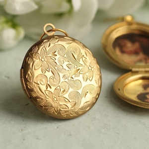May include: A round gold-tone metal locket with an intricate floral and swirl engraving on the front. One locket is closed, while the other is open, revealing two circular interior compartments that each contain a small, blurry photograph of people.
