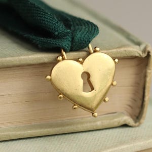 May include: A gold heart-shaped bookmark with a keyhole in the center. The bookmark is attached to a dark green ribbon.
