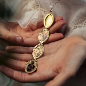 Puede incluir: Un collar con relicario de metal dorado que presenta una cadena vertical de cuatro marcos ovalados conectados. El marco superior está vacío con un interior texturizado, mientras que los tres marcos inferiores contienen retratos en tono sepia.