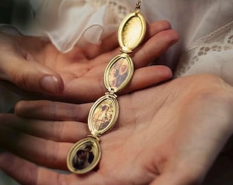 May include: A gold-toned metal locket necklace featuring a vertical chain of four connected oval frames. The top frame is empty with a textured interior, while the three lower frames contain small, sepia-toned portrait photographs of people.