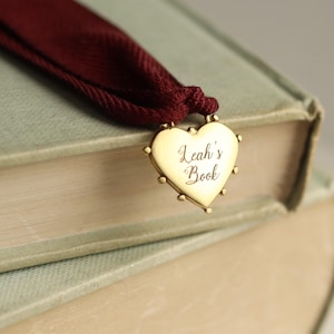 May include: A gold heart-shaped bookmark with the inscription "Leah's Book" attached to a burgundy ribbon.