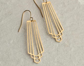 Puede incluir: Un par de pendientes dorados de estilo Art Déco. Cada pendiente presenta una parte superior rectangular con líneas verticales y formas geométricas en la parte inferior. Los pendientes tienen un cierre de gancho.