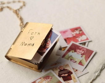May include: A gold-toned metal locket shaped like a miniature book, suspended from a matching chain. The cover is engraved with the text 'Fern ♡ Mama'. Inside the locket are several small, square photographic prints featuring children.