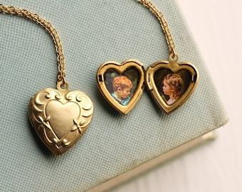 May include: Gold-colored heart-shaped locket necklace, one closed and one open, revealing two small photographs. The locket has an ornate design and hangs on a delicate chain. The open locket displays two children's portraits.