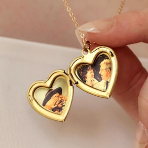 Op de afbeelding: Een goudkleurige hartvormige medaillonketting, open om twee kleine foto's te laten zien. Het medaillon hangt aan een fijne ketting. De foto's tonen twee verschillende afbeeldingen van mensen.