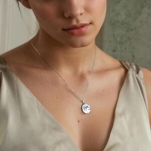 Peut inclure: Un collier pendentif argent&eacute; avec un charm en forme de goutte d'eau textur&eacute;. La cha&icirc;ne d&eacute;licate et le pendentif sont pr&eacute;sent&eacute;s sur un fond neutre. Le collier est un bijou simple et &eacute;l&eacute;gant.