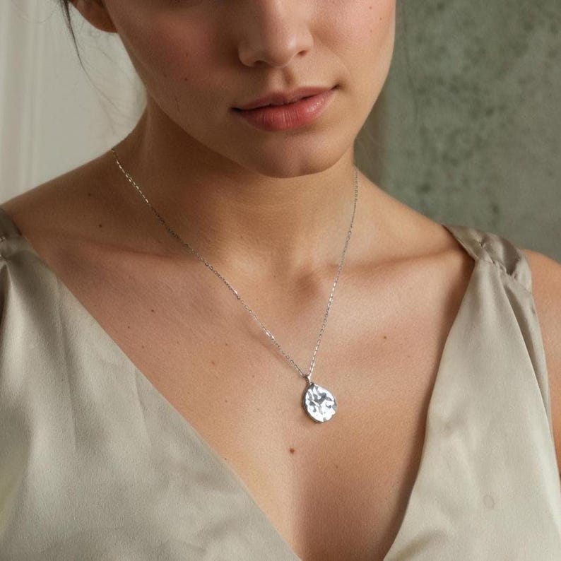 Peut inclure: Un collier pendentif argent&eacute; avec un charm en forme de goutte d'eau textur&eacute;. La cha&icirc;ne d&eacute;licate et le pendentif sont pr&eacute;sent&eacute;s sur un fond neutre. Le collier est un bijou simple et &eacute;l&eacute;gant.