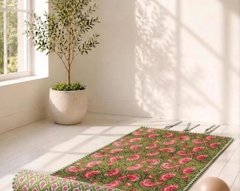 May include: A rectangular floor mat featuring a green base with a repeating pink floral pattern. The mat is partially rolled at one end, revealing a secondary green and pink geometric print on the underside. It includes decorative fringe edges.