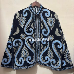 Peut inclure: Veste en velours noir avec broderies bleues claires et argentées. La veste présente un col montant et une doublure rayée. Le texte "ThreadsArtt" est visible sur le devant de la veste.