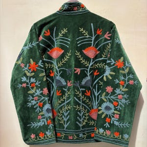 May include: A dark green velvet jacket with intricate floral embroidery in shades of orange, pink, and blue. The jacket features a high collar and detailed patterns on the back and sleeves, creating a bohemian aesthetic.