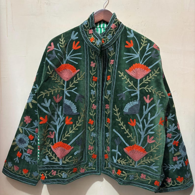 May include: A dark green velvet jacket with floral embroidery in shades of orange, pink, blue, and green. The jacket has a high collar and long sleeves. The lining is striped green and white.