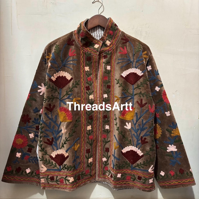 May include: Brown velvet jacket with vibrant floral embroidery. The jacket has a high collar and a full-length zip. The embroidery features red, yellow, and blue flowers. The text "ThreadsArtt" is visible on the jacket.
