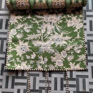 May include: A quilted fabric roll featuring a green background with a white floral pattern and a top section displaying a repeating tiger print. The edges are finished with a striped trim, and three sets of fabric ties hang from the bottom edge.
