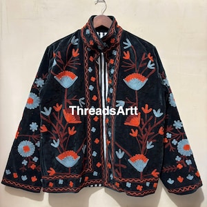 Op de afbeelding: Zwarte jas met bloemenborduurwerk in rood, oranje en blauw. De jas heeft een hoge kraag en lange mouwen. De tekst "ThreadsArtt" is zichtbaar op de voorkant van de jas.