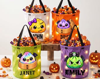 Op de afbeelding: Vier cilindervormige Halloween-snoepemmers met zwarte hengsels en interne verlichting. De witte emmer toont een pompoen, de oranje een paarse dumpling, de groene een regenboog-dumpling en de paarse emmer een groene dumpling met namen.