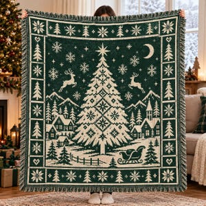 Könnte beinhalten: Eine dunkelgrüne und cremefarbene Webdecke mit einem zentralen Weihnachtsbaum, springenden Rentieren, einer Mondsichel und einer verschneiten Dorflandschaft. Der Rand zeigt ein wiederkehrendes Muster aus Tannen, Schneeflocken und Herzen.