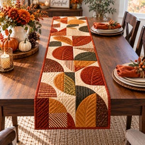 May include: A rectangular quilted table runner featuring a geometric pattern of semicircles and triangles in autumn colours including burnt orange, olive green, brown, and cream. The fabric displays various textures and leaf-like stitching patterns.