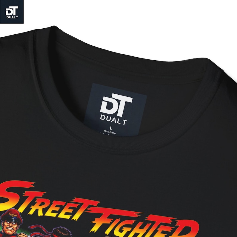 May include: A black crew neck t-shirt featuring a graphic print with the text Street Fighter in a red and yellow gradient font. The inner neck label displays the DUAL T logo, the size L, and the text 100% Cotton on a dark blue background.