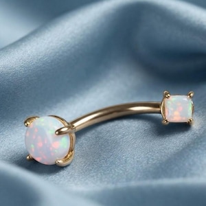 May include: A curved barbell body jewelry piece featuring a gold-toned metal shaft. One end is capped with a round, iridescent white opal stone, while the other end features a square-shaped, iridescent white opal stone held by four prongs.