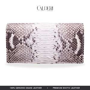 Può includere: Un portafoglio in pelle di serpente bianca e grigia con patta. Il portafoglio ha un motivo strutturato e il marchio "CALDERI" è in alto. La parte inferiore dell'immagine recita "100% VERA PELLE DI SERPENTE".