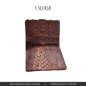Op de afbeelding: Een bruine slangenleren portemonnee met een getextureerd, schubachtig patroon. De portemonnee is open en onthult de binnenkant. De merknaam "CALDERI" staat bovenaan. De tekst "100% GENUINE SNAKE LEATHER" staat onderaan.