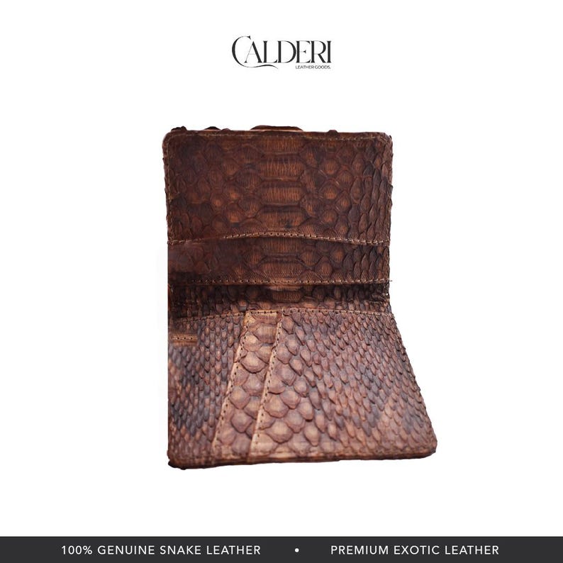 Op de afbeelding: Een bruine slangenleren portemonnee met een getextureerd, schubachtig patroon. De portemonnee is open en onthult de binnenkant. De merknaam "CALDERI" staat bovenaan. De tekst "100% GENUINE SNAKE LEATHER" staat onderaan.