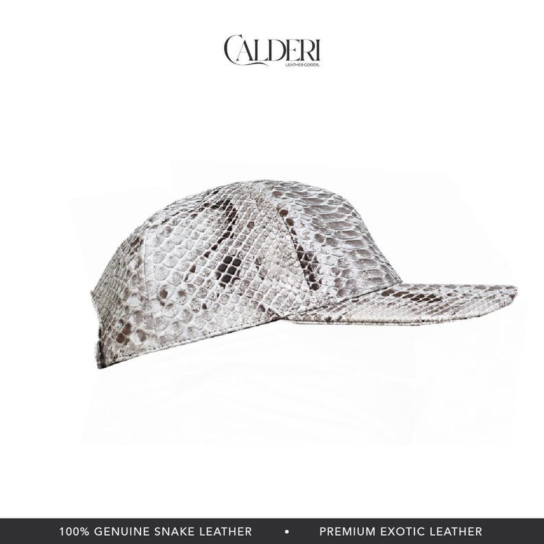 May include: A baseball cap crafted from genuine snake leather, showcasing a white and grey snakeskin design. The brand name "CALDERI" is visible at the top. The bottom of the image states "100% GENUINE SNAKE LEATHER" and "PREMIUM EXOTIC LEATHER."