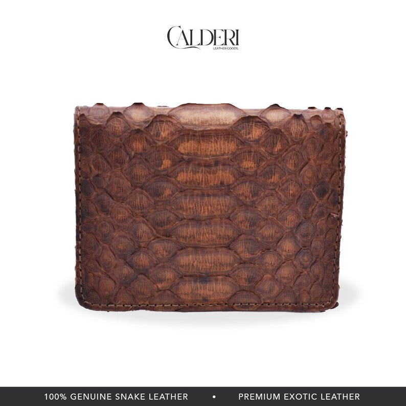 Op de afbeelding: Een bruine, rechthoekige portemonnee van echt slangenleer. De portemonnee heeft een getextureerd, geschubd patroon en is gesloten. De merknaam "CALDERI" staat bovenaan. De onderkant van de afbeelding luidt "100% ECHT SLANGENLEER" en "PREMIUM EXOTISCH LEER."