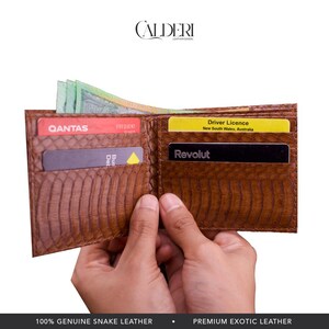 May include: Open brown snake leather wallet with multiple card slots and cash. The wallet is held open, displaying cards and Australian currency. The wallet has the brand name "CALDERI" at the top.