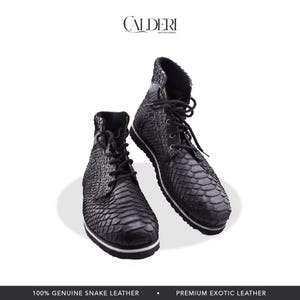 May include: Black leather boots with a snakeskin texture. The boots feature black laces, metal eyelets, and a white stripe on the sole. The brand name "CALDERI LEATHER GOODS" is visible at the top.