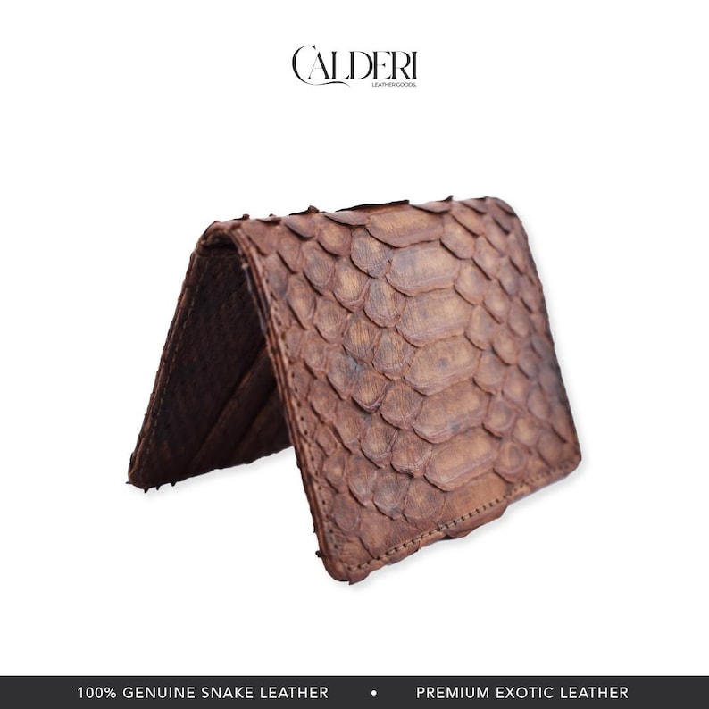 Op de afbeelding: Een bruine slangenhuid portemonnee, open. De portemonnee heeft een getextureerd, geschubd patroon. De merknaam "CALDERI" staat bovenaan. De onderkant van de afbeelding luidt "100% GENUINE SNAKE LEATHER" en "PREMIUM EXOTIC LEATHER."