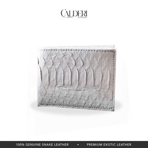 May include: A white bi-fold wallet made of genuine snake leather. The wallet has a textured, scale-like pattern and is rectangular in shape. The brand name "CALDERI" is visible at the top. The bottom of the image reads "100% GENUINE SNAKE LEATHER".