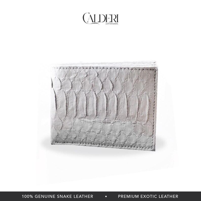 May include: A white bi-fold wallet made of genuine snake leather. The wallet has a textured, scale-like pattern and is rectangular in shape. The brand name "CALDERI" is visible at the top. The bottom of the image reads "100% GENUINE SNAKE LEATHER".