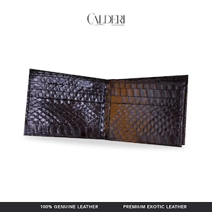 Może przedstawiać: Otwarty, ciemnobrązowy skórzany portfel o fakturze skóry krokodyla. Portfel ma wiele przegródek na karty i przegrodę na banknoty. Marka "CALDERI" jest widoczna u góry. Na dole obrazu widnieje napis "100% GENUINE LEATHER" i "PREMIUM EXOTIC LEATHER."