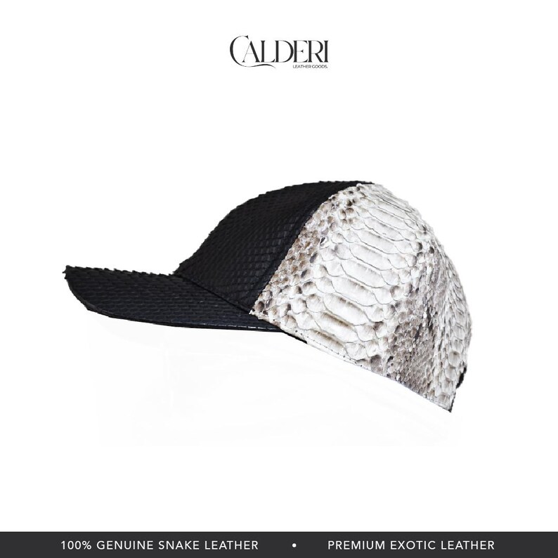May include: A baseball cap in black and white, crafted from genuine snake leather. The cap has a textured black front and a white and grey snakeskin pattern on the side. The brand name "CALDERI" is displayed.