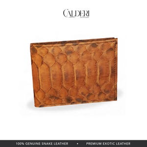 May include: A brown bi-fold wallet made of genuine snake leather. The wallet has a textured, scale-like pattern and a rectangular shape. The brand name "CALDERI" is visible at the top. The bottom of the image reads "100% GENUINE SNAKE LEATHER" and "PREMIUM EXOTIC LEATHER."