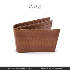 May include: A brown bi-fold wallet made of genuine snake leather. The wallet has a textured, scaly pattern and is open to reveal the interior card slots. The brand name "CALDERI" is displayed at the top.