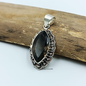 May include: Smoky quartz pendant with a silver bail and ornate filigree setting. The dark gemstone is oval-shaped and faceted, set against a wooden background. The pendant is approximately 1.5 inches long.