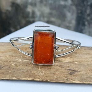 May include: A silver bracelet featuring a rectangular amber-colored stone. The stone is set in a silver frame and the bracelet has a delicate, open design. The text "Shreejaipursilver205" is visible on the image.