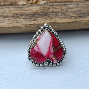 Peut inclure: Bague en forme de cœur avec un anneau en argent et une pierre composite. La pierre présente un mélange de couleurs rouge, blanc et or. La bague a une bordure perlée et un motif de corde torsadée. Le texte "Shreejaipursilver205" est visible.