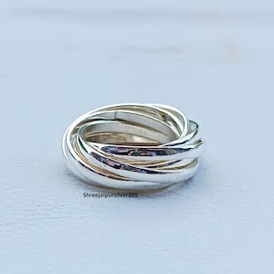 Puede incluir: Un anillo de plata con múltiples bandas entrelazadas. El anillo está hecho de metal pulido y tiene una superficie brillante y reflectante. Es una pieza de joyería.