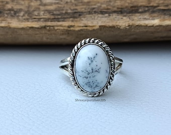 Puede incluir: Un anillo de plata con una piedra ovalada blanca con motas grises. La piedra está engastada en un borde retorcido en forma de cuerda. El anillo está sobre una superficie clara con un fondo de madera. El texto "Shreejaipursilver205" es visible.