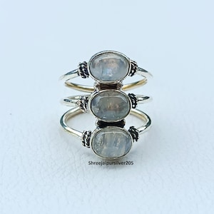 May include: Three silver rings stacked vertically, each with an oval, iridescent gemstone. The rings have a simple band design with decorative accents near the gemstone settings. The text "Shreejaipursilver205" is visible.